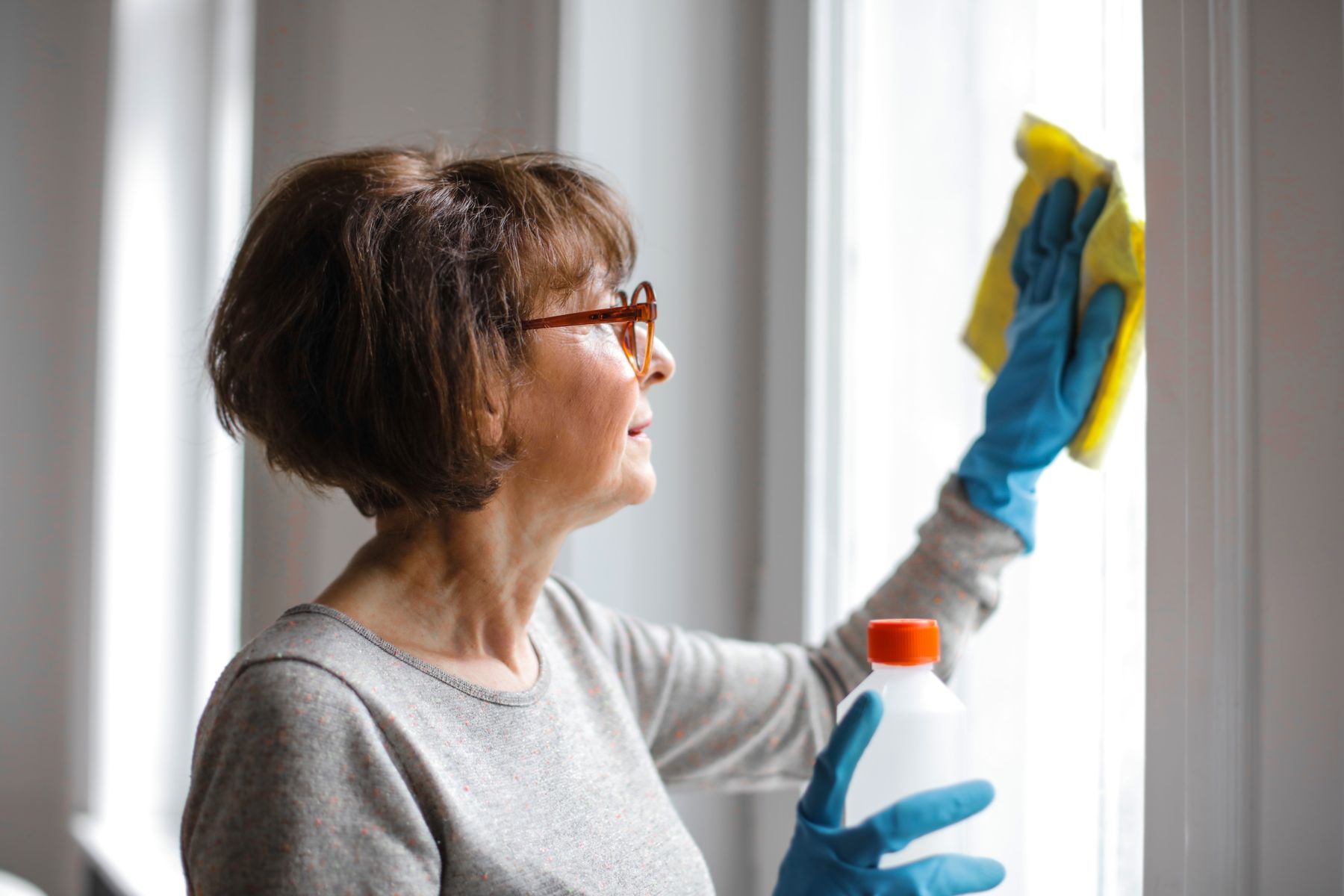 Fensterreinigung mit Handschuhen und Sprühflasche an einem hellen Fenster