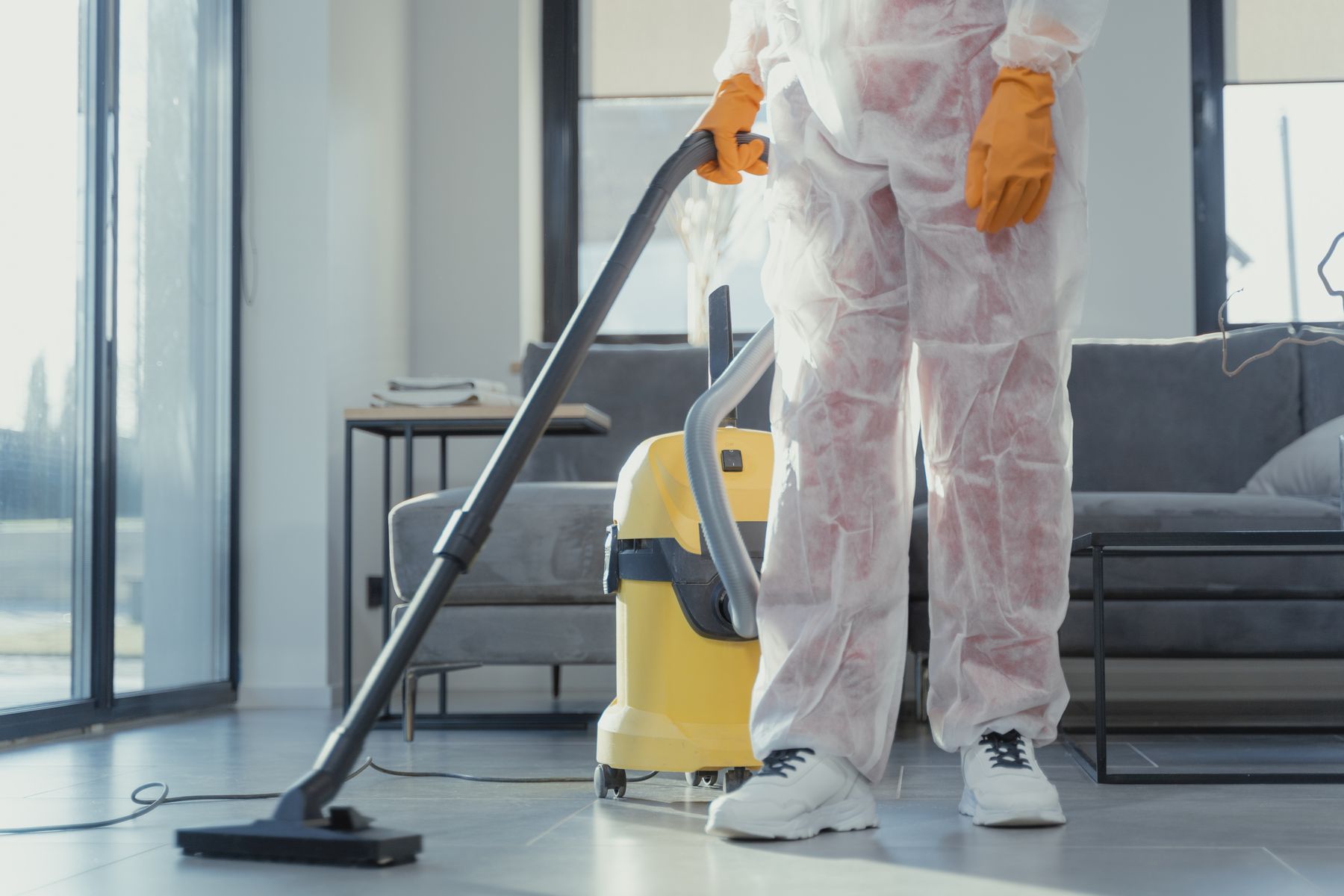 Reinigungskraft im Schutzanzug saugt mit einem Industriesauger einen Wohnraum