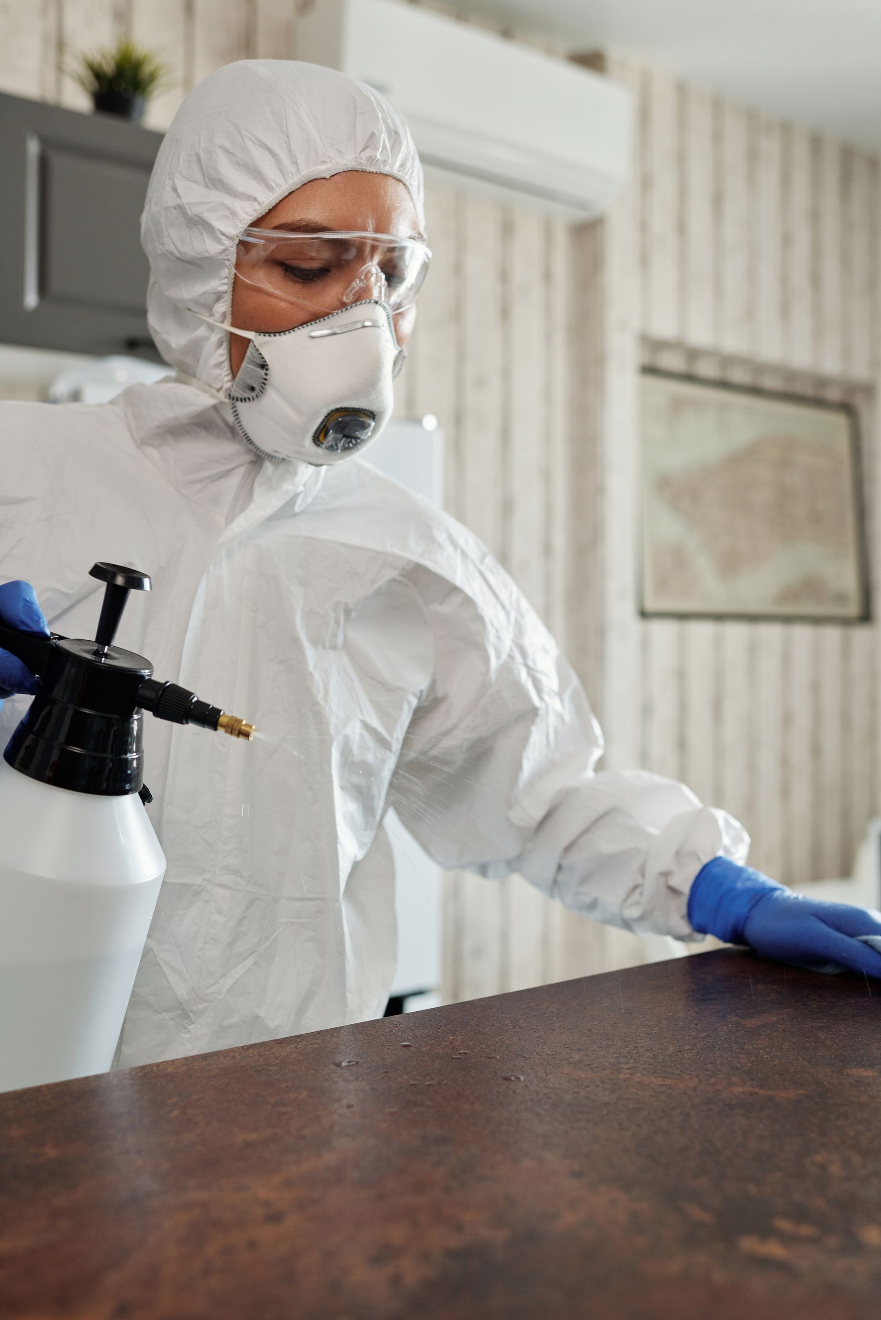 Reinigungskraft in Schutzkleidung desinfiziert eine Oberfläche